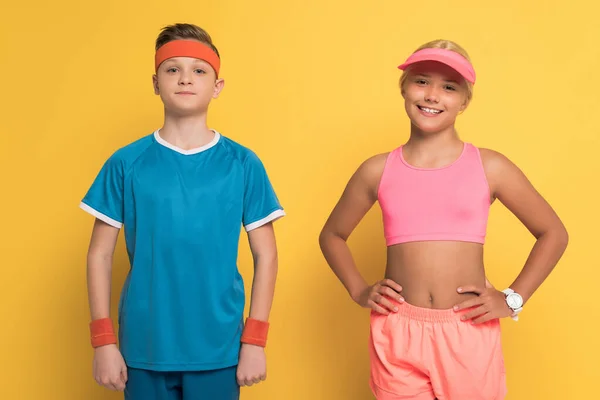 Niños sonrientes en ropa deportiva mirando a la cámara sobre fondo amarillo - foto de stock