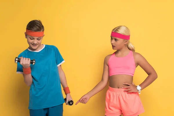 Kid pointing with finger and talking with friend in sportswear during work out on yellow background — Stock Photo