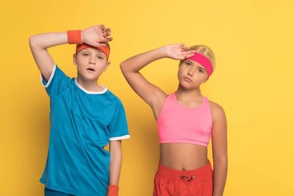 Niños cansados en ropa deportiva tocando cabezas sobre fondo amarillo - foto de stock