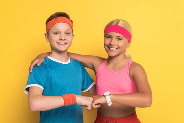 Niños sonrientes en ropa deportiva abrazando y haciendo golpe de puño sobre fondo amarillo - foto de stock