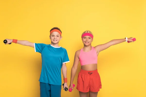 Crianças sorridentes no treinamento de sportswear com halteres no fundo amarelo — Fotografia de Stock