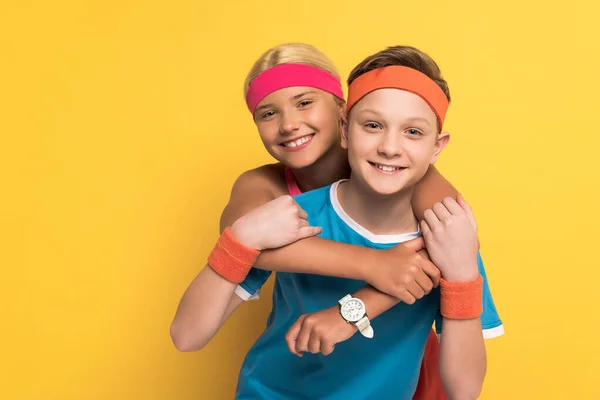 Niños sonrientes en ropa deportiva abrazando y mirando a la cámara en el fondo amarillo - foto de stock