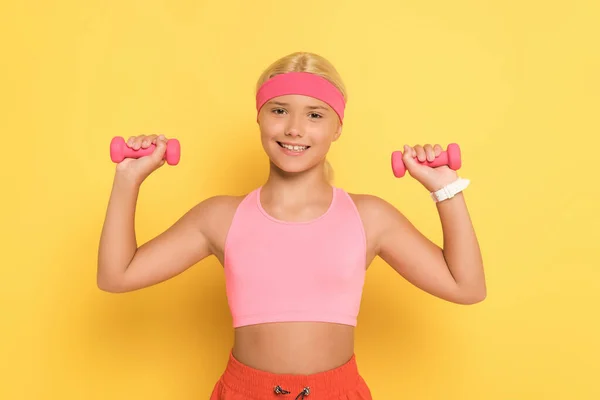 Lächelnde Frühchen-Sportlerin beim Training mit Kurzhanteln auf gelbem Hintergrund — Stockfoto