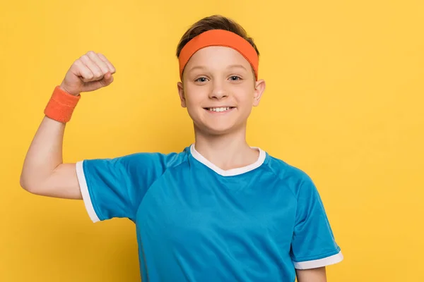 Lächelndes Kind in Sportkleidung mit starker Geste auf gelbem Hintergrund — Stockfoto