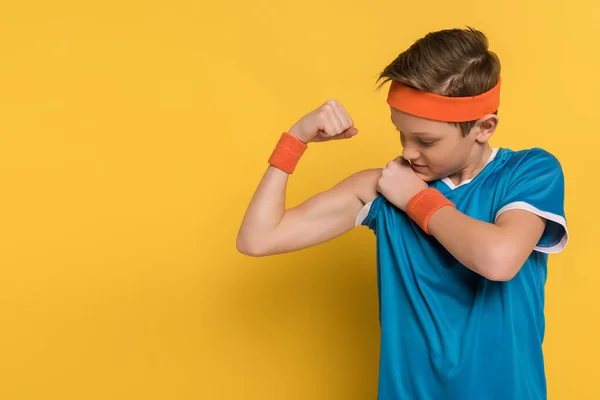 Niño en ropa deportiva mostrando músculos sobre fondo amarillo - foto de stock
