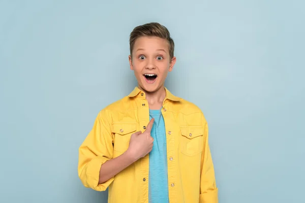 Surprised and cute kid pointing with finger on blue background — Stock Photo