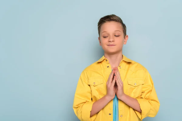 Smiling and cute kid showing praying hands on blue background — Stock Photo