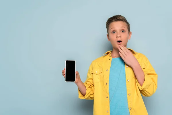 Enfant choqué tenant smartphone avec écran blanc sur fond bleu — Photo de stock