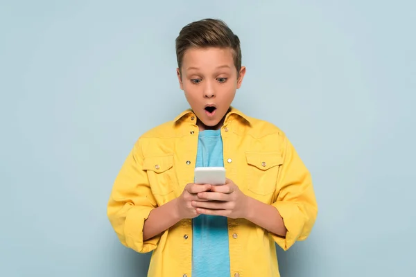 Shocked kid using and looking at smartphone on blue background — Stock Photo