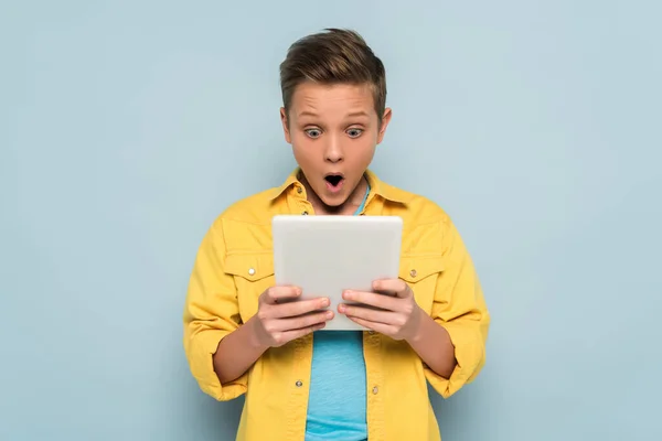 Garoto chocado usando e olhando para tablet digital em fundo azul — Fotografia de Stock