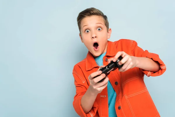 KYIV, UKRAINE - JANUARY 21, 2020: shocked kid playing with joystick on blue background — Stock Photo