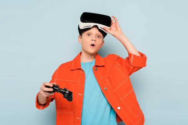 KIEW, UKRAINE - 21. JANUAR 2020: Schockiertes Kind mit Virtual-Reality-Headset mit Joystick auf blauem Hintergrund — Stockfoto