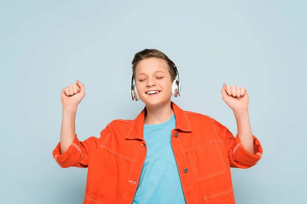 Lächelnder Junge mit Kopfhörern, der Musik auf blauem Hintergrund hört — Stockfoto