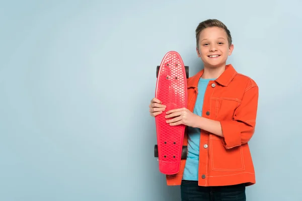 Enfant souriant tenant penny conseil et regardant la caméra sur fond bleu — Photo de stock