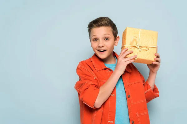 Sonriente y lindo niño sosteniendo caja de regalo sobre fondo azul - foto de stock
