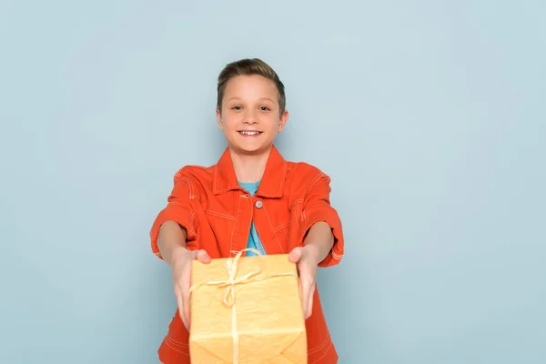 Sonriente y lindo niño sosteniendo caja de regalo sobre fondo azul - foto de stock