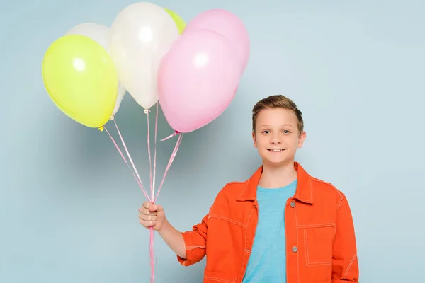 Усміхнена дитина тримає повітряні кулі і дивиться на камеру на синьому фоні — стокове фото