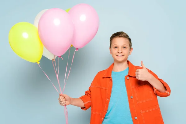 Bambino sorridente che tiene i palloncini e mostra come su sfondo blu — Foto stock