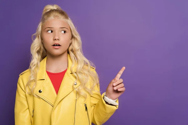 Shocked and cute kid pointing with finger on purple background — Stock Photo