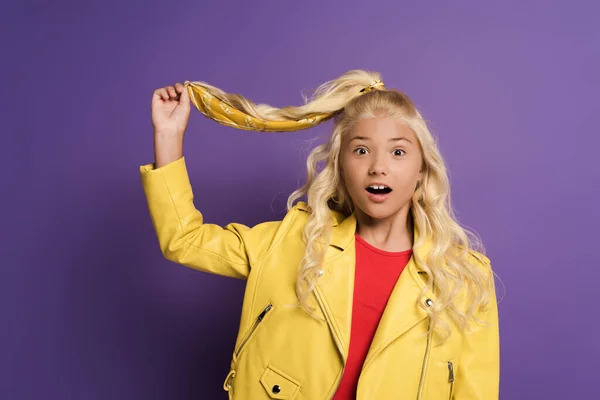 Chocado y lindo niño tocando el pelo sobre fondo púrpura - foto de stock