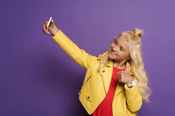 Bambino sorridente prendendo selfie e mostrando come su sfondo viola — Foto stock