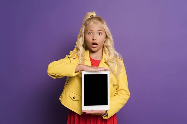 Шокированный ребенок держит цифровой планшет с места для копирования на фиолетовом фоне — стоковое фото