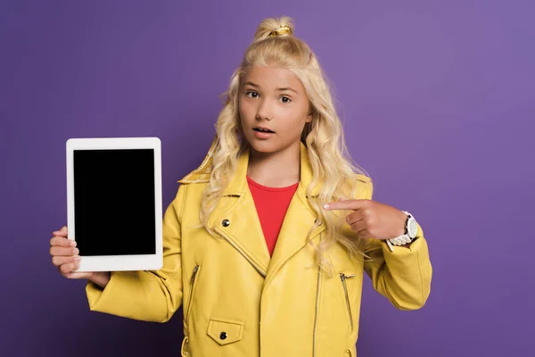 Schockiertes Kind zeigt mit dem Finger auf digitales Tablet mit Kopierplatz auf lila Hintergrund — Stockfoto