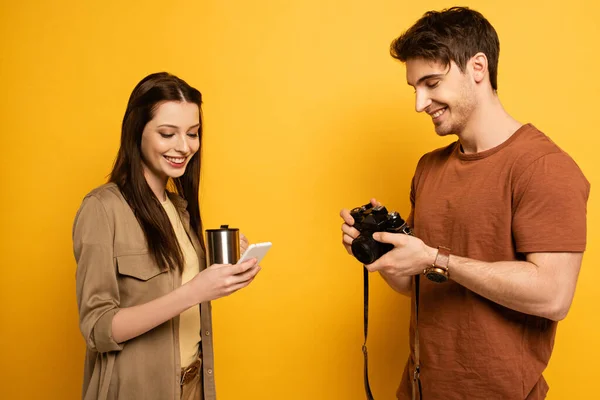 Couple of smiling travelers holding photo camera, smartphone and cup of coffee on yellow — Stock Photo