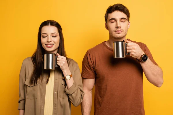 Par de turistas felizes segurando xícaras de café com prazer em amarelo — Fotografia de Stock