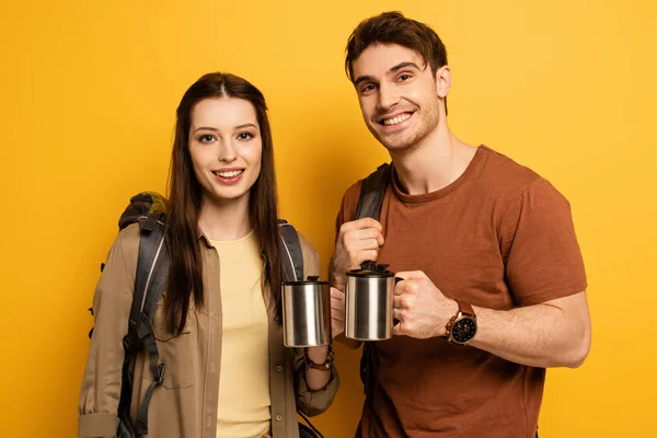 Ein paar lächelnde Touristen mit Rucksäcken, die Tassen mit Kaffee auf gelb halten — Stockfoto