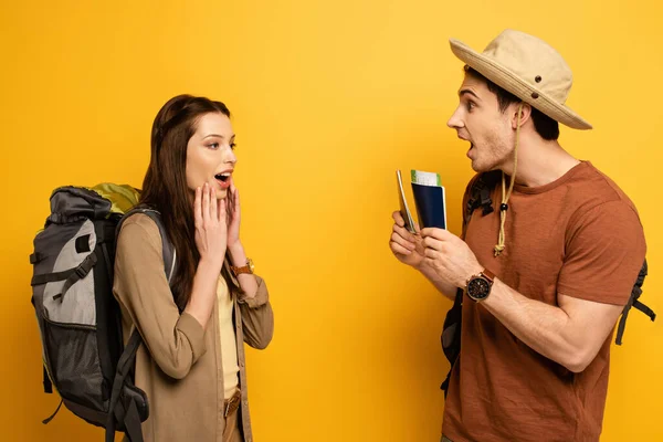 Excited girlfriend with backpack and boyfriend holding passports and tickets on yellow — Stock Photo