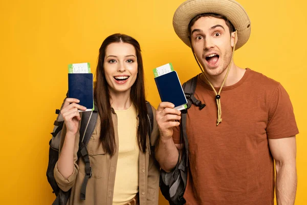 Couple of excited travelers with backpacks holding passports and tickets on yellow — Stock Photo