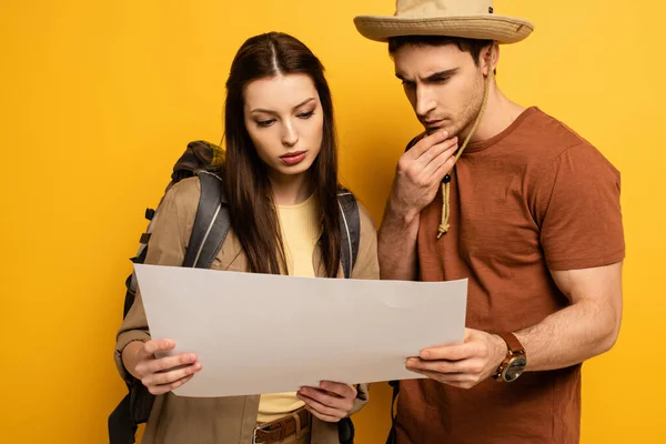 Couple of thoughtful tourists with backpacks looking at map on yellow — Stock Photo