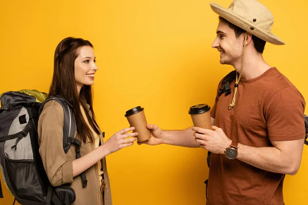 Couple of happy travelers with backpacks holding coffee to go on yellow — Stock Photo