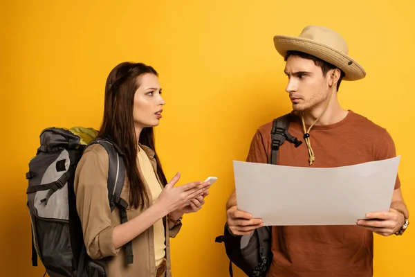 Couple de touristes confus avec sacs à dos et smartphone regardant la carte sur jaune — Photo de stock