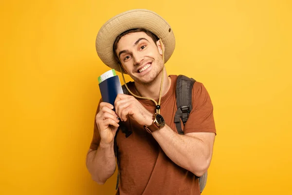 Emotionaler Tourist mit Hut und Rucksack mit Pass und Ticket auf gelb — Stockfoto
