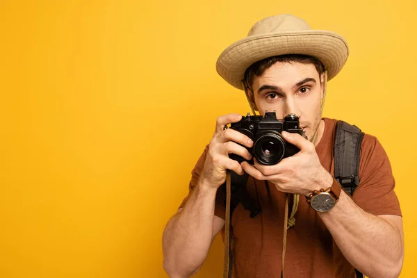 Turista bonito em chapéu com mochila tirando foto na câmera no amarelo — Fotografia de Stock