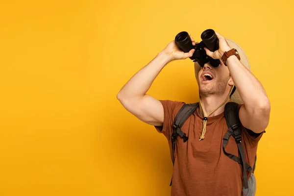 Apuesto viajero pensativo mirando a través de prismáticos en amarillo - foto de stock