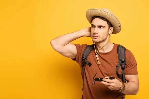 Handsome pensive traveler holding compass on yellow — Stock Photo