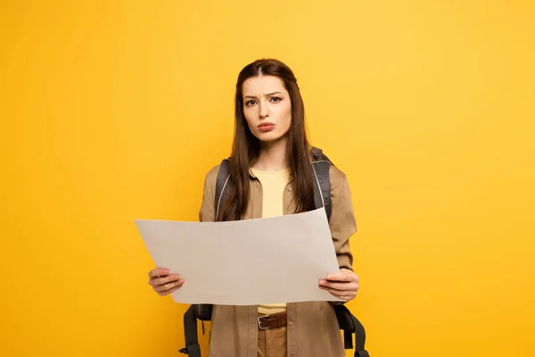 Pensive female tourist with backpack holding map, isolated on yellow — Stock Photo