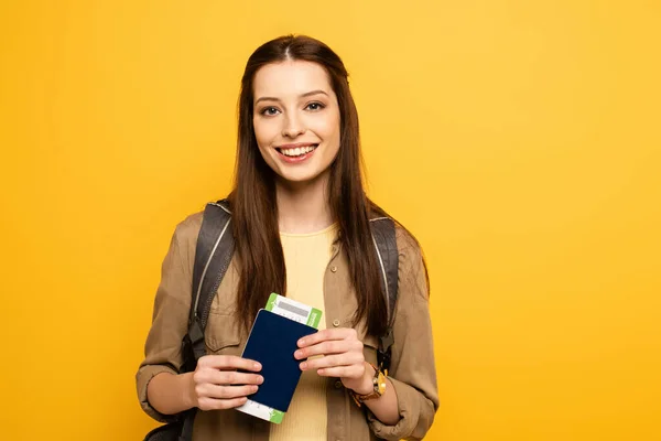 Turista sonriente con mochila con pasaporte y billete, aislado en amarillo - foto de stock