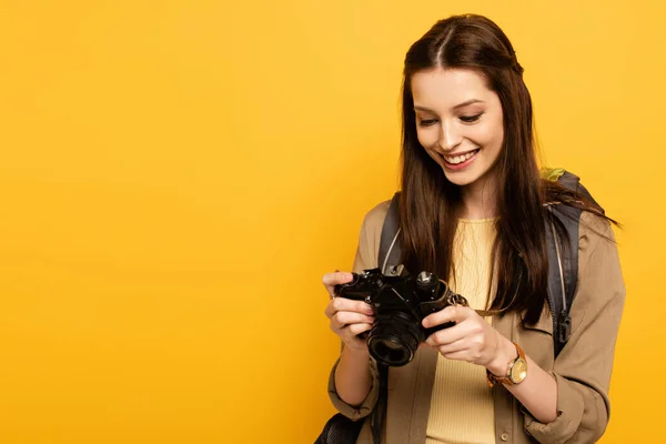 Attraente felice turista femminile con zaino tenendo fotocamera fotografica su giallo — Foto stock