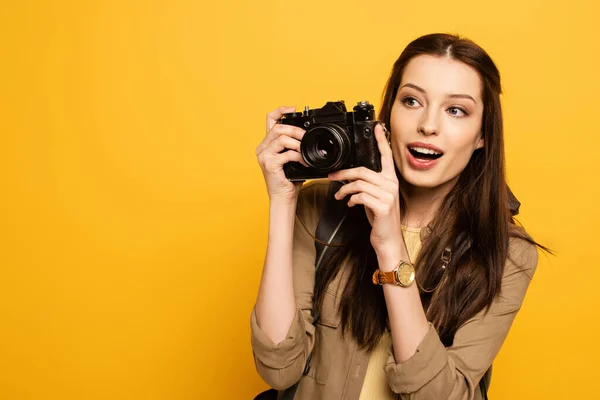 Touriste féminine surprise avec sac à dos tenant appareil photo sur jaune — Photo de stock