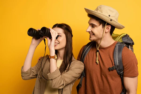 Couple de voyageurs souriants avec sac à dos et jumelles sur jaune — Photo de stock