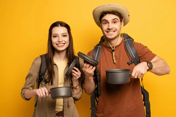 Pareja de turistas alegres con mochilas sosteniendo ollas en amarillo - foto de stock