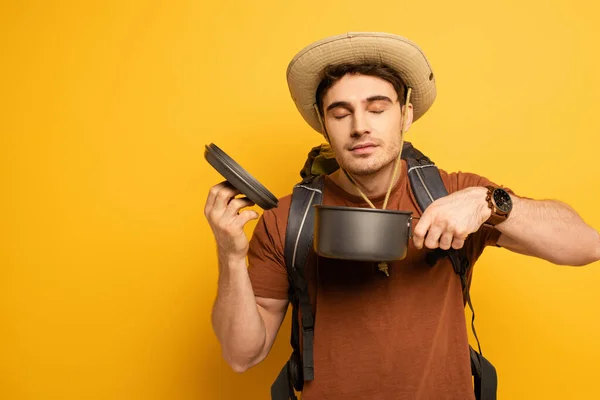 Handsome traveler smelling food in pot on yellow — Stock Photo