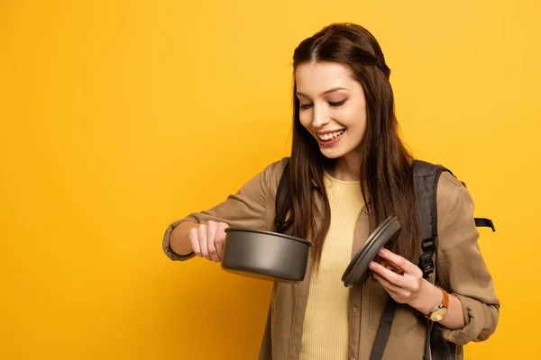 Attractive smiling female traveler with backpack holding pot on yellow — Stock Photo