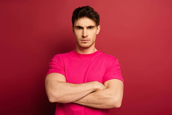 Portrait of serious man with crossed arms in pink t-shirt on red — Stock Photo