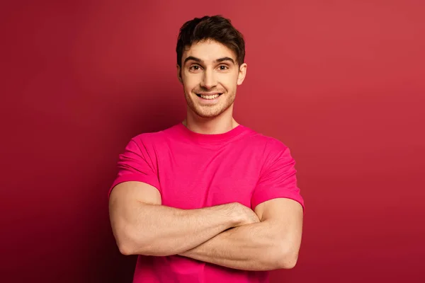 Porträt eines lächelnden Mannes in rosa T-Shirt mit verschränkten Armen auf rot — Stockfoto