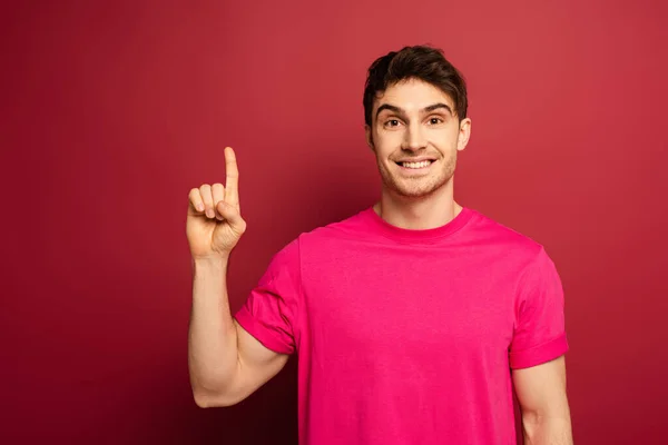 Portrait of smiling man in pink t-shirt pointing up on red — Stock Photo